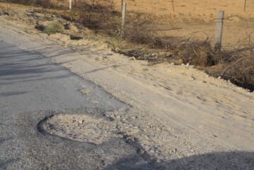 Bad road, cracked asphalt with potholes and big holes. Potholes on the road with stones on the asphalt. The asphalt surface is destroyed on the road. Bad condition of the road - 778663637