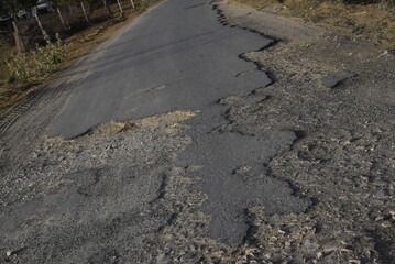 Bad road, cracked asphalt with potholes and big holes. Potholes on the road with stones on the asphalt. The asphalt surface is destroyed on the road. Bad condition of the road - 778663667