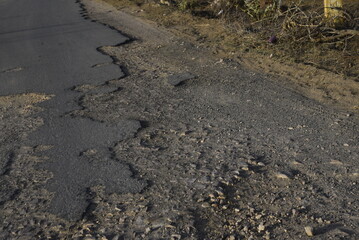 Bad road, cracked asphalt with potholes and big holes. Potholes on the road with stones on the asphalt. The asphalt surface is destroyed on the road. Bad condition of the road - 778663675