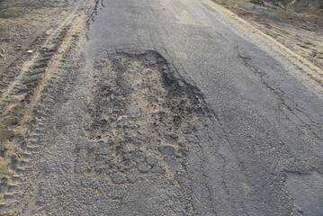 Bad road, cracked asphalt with potholes and big holes. Potholes on the road with stones on the asphalt. The asphalt surface is destroyed on the road. Bad condition of the road