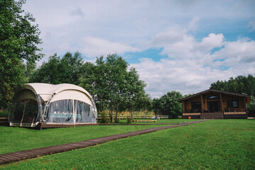 Fototapeta na wymiar Glamping Dome and Wooden Cabin in Countryside. A spacious glamping dome next to a cozy wooden cabin offers a luxurious camping experience in the tranquil countryside setting.