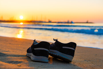Pair of shoes lying on the sand at the beach at sunset or sunrise. Freedom concept, walking by the seaside, vacation. Teal and orange colors with copy space. High quality photo