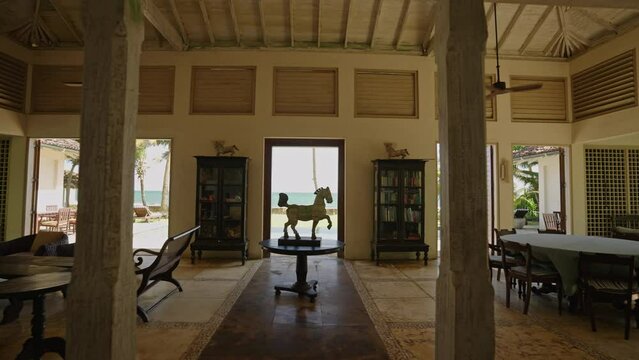 Statue of white horse in center of living room with vintage furniture in luxury retro villa. Room with art objects and access to pool with palm trees in oceanfront resort on tropical island.
