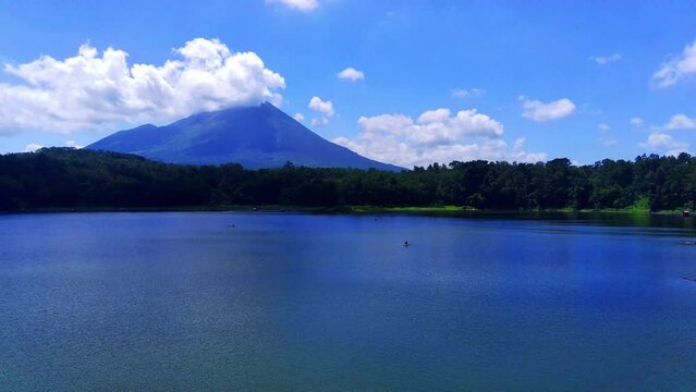 a crystal clear lake Ranu Klakah, Lumajang with a majestic mountain in the background. Lush greenery surrounds the base of the mountain in East Java, Indonesia.