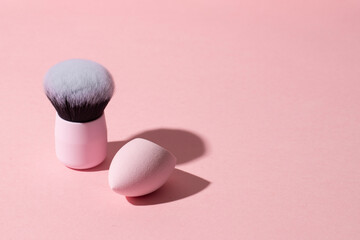 Cosmetic minimalist make up set, kabuki brush and sponge blender on pink background , copy space