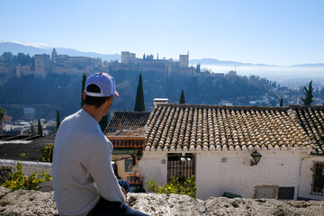 Turismo en ciudad de Granada, Andalucía, hombre de espaldas con gorra blanca mirando la Alhambra