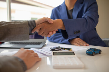 customer and car dealer shake hands after agreeing to sales contract before making contract payment...
