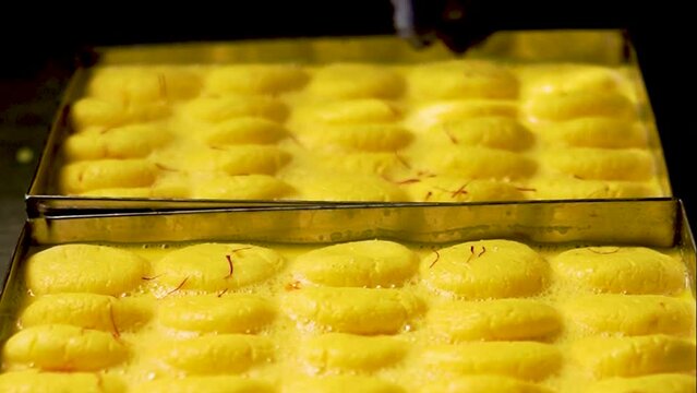 Delicious Rasmalai, Rossomalai, Roshmolai is popular Indian dessert. chef droping kesar on sweet made with cottage cheese and milk to celebrate festivals of India like Diwali, Holi, Ganesh Chaturthi.