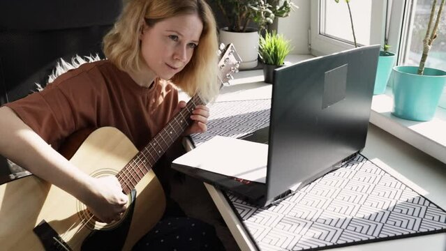 Learning guitar online, woman practicing at home, acoustic instrument lesson, laptop education