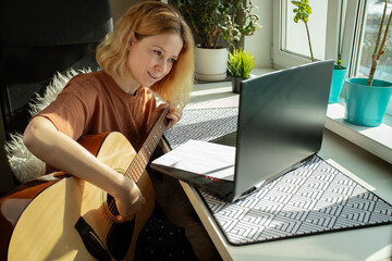 Learning guitar online, woman practicing at home, acoustic instrument lesson, laptop education