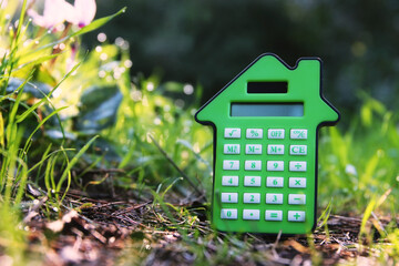 Calculator in the shape of a house in nature. Idea of expenses and real estate - 778709049