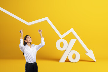Happy young businesswoman with falling white chart arrow with percent icon on yellow background. Falling interest rates and mortgage concept.