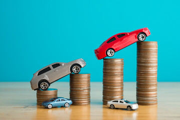 Car model on stacked coins as growth chart graph on wooden table with blue background. Business, financial and economy concept. Car price increase in inflation, money savings for new or used car.