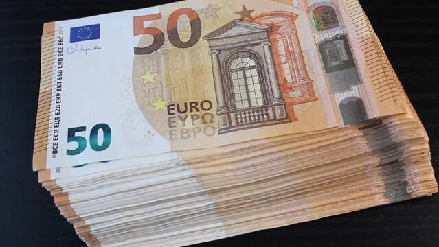 A stack of 50 euro banknotes falls freely on the surface of a black office desk
