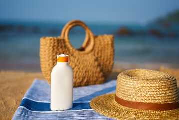 Bottle of high SPF sunscreen, straw hat, on towel at sunny beach. Summer skin care essentials by...
