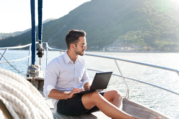 Man working on yacht office with laptop. Summer traveling on sailboat with insurance. Traveler...