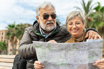 Happy wife and husband enjoying retirement together - Senior married couple of tourists with city street with map