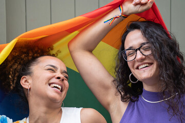 Headshot of lesbian young couple with positive mood laughing and smiling with LGBTQ rainbow flag