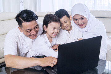 Happy muslim family of four using laptop watching streaming video