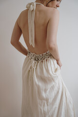 Back view of young woman in neutral cream beige evening dress against white wall. Minimal chic...