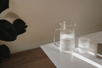 Decanter and glass of pure clean water on table with elegant sunlight reflections and shadow. Healthy lifestyle