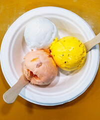 Top view of 3 flavors of ice cream scoops in a white bowl on a mustard colored background