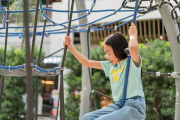 Obraz premium Joyful Asian girl having enjoy and fun playing on a zip line in an adventure park outdoors on the playground.