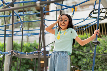 Joyful Asian girl having enjoy and fun playing on a zip line in an adventure park outdoors on the playground.