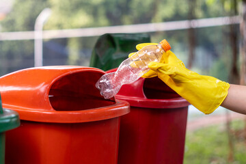 Hand throwing plastic bottle into trash bin, waste disposal concept.