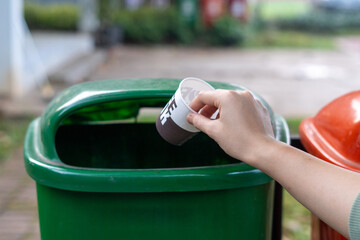 Hand throwing plastic cup into trash bin, waste disposal concept.