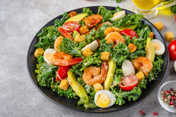 Plate of healthy salad with shrimps, kale cabbage, avocado, tomatoes, croutons and quail eggs on gray table. Tasty diet food for lunch