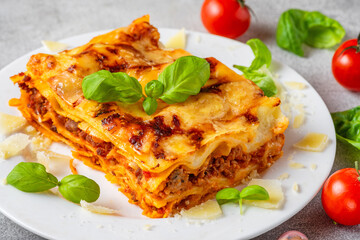 Close up of meat lasagna with fresh basil, tomatoes and parmesan cheese in a plate. Italian cuisine. Delicious food for dinner - 778778436