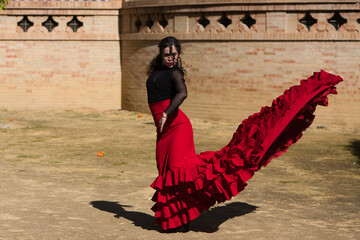 Beautiful woman dancing flamenco in Seville, Spain. She wears a red and black dress typical of a flamenco dancer with a lot of art, you can see the movement in the air of the frilly dress.