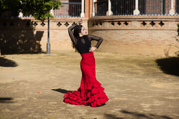 Beautiful woman dancing flamenco in Seville, Spain. She is wearing a red and black gypsy dress and dancing flamenco with a lot of art. In the background a monument with arches and columns.