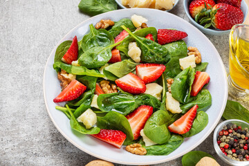 Green salad with spinach, strawberries, parmesan cheese, walnuts and olive oil in a plate with fork. Healthy summer vegetarian food for lunch. Tasty appetizer - 778782226