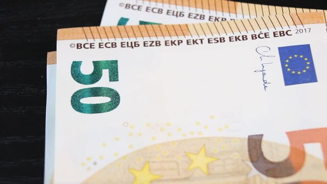 A man counts out 50 euro banknotes and places them one by one on a black office desk