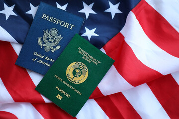 Passport of Nigeria with US Passport on United States of America folded flag close up - obrazy, fototapety, plakaty