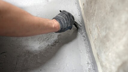 Brush with gray primer. A man paints the concrete floor in his bathroom with a gray brush....