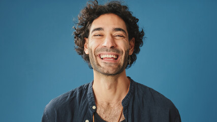 Close up, laughing attractive man with curly hair, dressed in blue shirt, crossing his arms and...