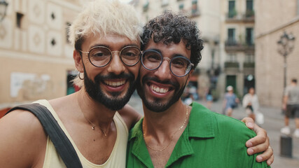 Homosexual couple stands hugging and looking at camera on street of old city