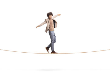 Full length portrait of a young man with curly hair walking on a tightrope and smiling