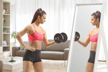 Fit young female exercising with a dumbbell in front of a mirror