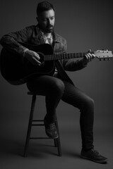 Black and white studio portrait of a handsome caucasian man in his 40s playing an acoustic guitar...