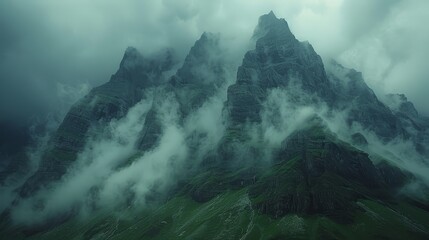   A towering mountain, shrouded in clouds with a few trees framing its base in the distance - obrazy, fototapety, plakaty