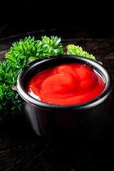 A vibrant red sauce in a black bowl, adorned with fresh green parsley on a dark background