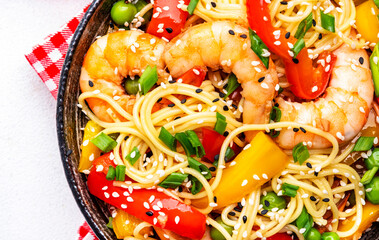 Spicy stir fry noodles with shrimps, colorful paprika, green pea, green onion and sesame seeds with ginger, garlic and soy sauce. White table background, close-up, top view