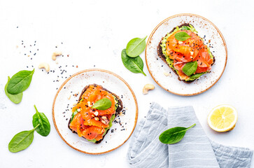 Avocado and salmon toast on rye bread with spinach, cashew and sesame seeds, white table background, top view