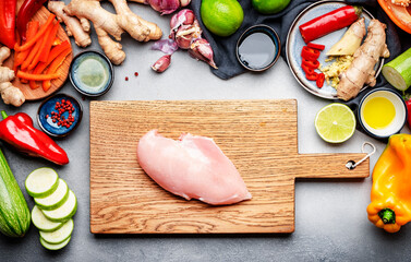 Food and cooking background. Gray table with chicken fillet. Paprika, zucchini, vegetables, spices and ingredients for cooking Asian dishes with ginger, garlic, soy sauce, top view