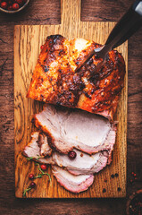 Baked festive pork butt or ham with herbs, spices and cranberries for sauce, served and sliced on cutting board, rustic wooden table background, top view