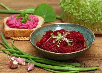 Traditional spicy beetroot salad with garlic and lemon juice. Bowl with beetroot salad decorated with garden cress, beetroot spread on whole grain bread at back.